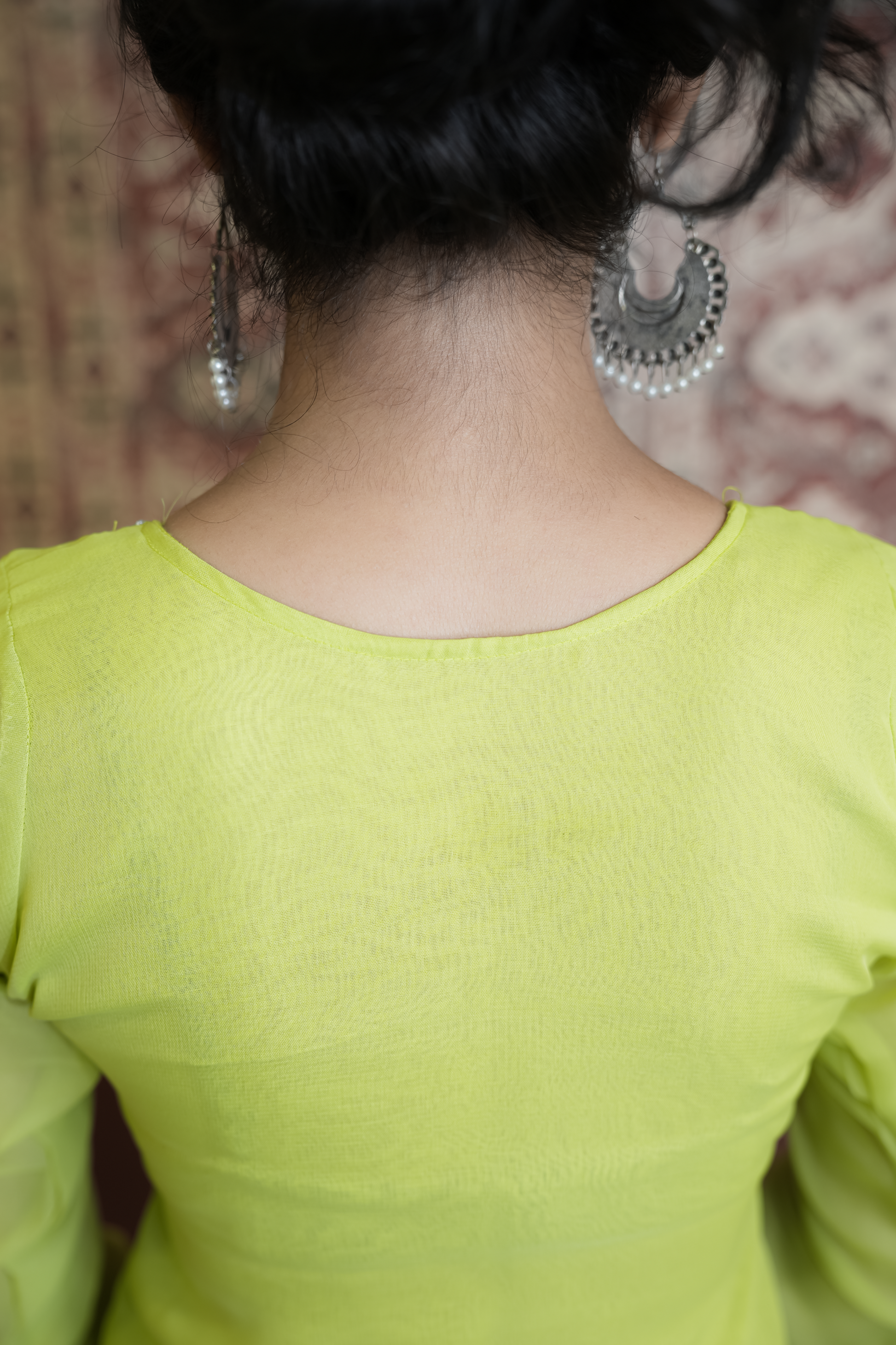 Person wearing a green top with silver earrings against a blurred background